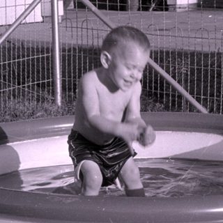 Toddler in an inflatable pool in a backyard.