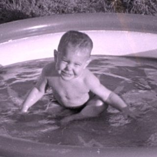 Child in an inflatable pool on a lawn.