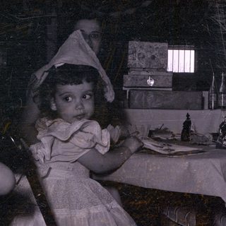 Two children in bonnets at a table with adults.