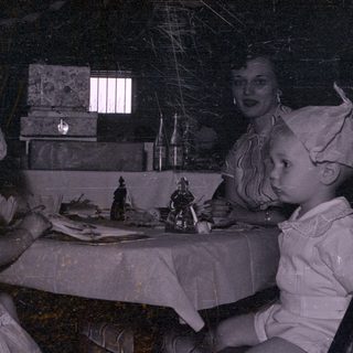 Two children in bonnets at a table with adults.
