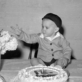 Child in a cap sitting behind a cake.