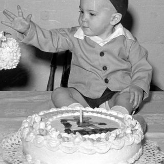 Child in a cap sitting behind a cake.
