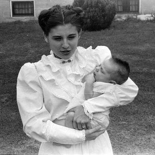 Woman holding an infant in a ruffled gown.