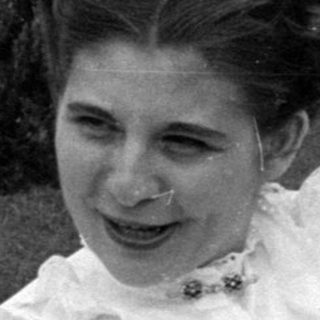 Woman in white dress holding an infant outdoors.