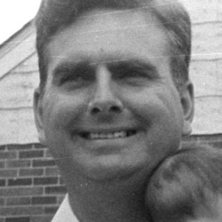 Man holding an infant in front of brick house.
