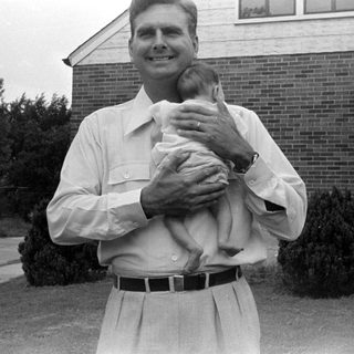 Man holding an infant in front of brick house.