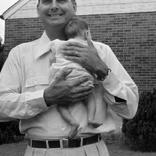 Man holding an infant in front of brick house.