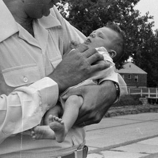 Man holding an infant outdoors near a house.