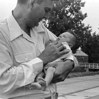 Man holding an infant outdoors near a house.