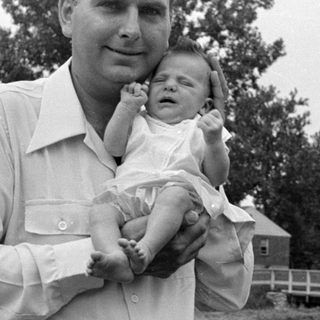 Man holding a sleeping infant in a residential setting.