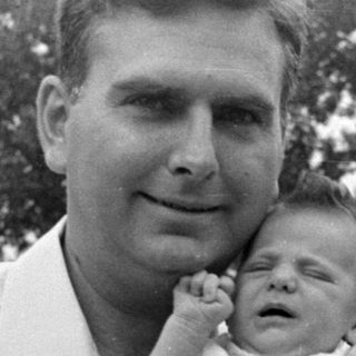 Man holding a sleeping infant in a residential setting.