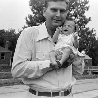 Man holding a sleeping infant in a residential setting.