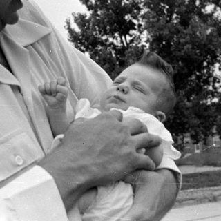 Man in white shirt holding a sleeping infant.
