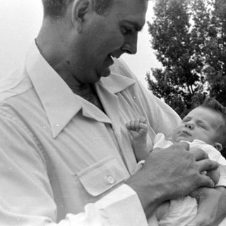 Man in white shirt holding a sleeping infant.