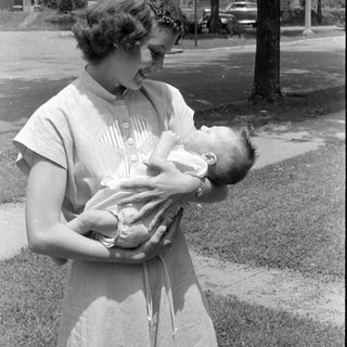 Woman holding an infant outdoors in black and white.