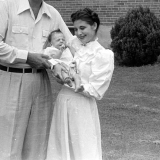 Man, woman, and infant in front of brick house.