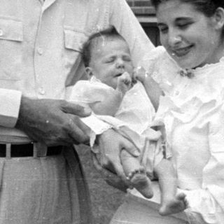 Man, woman, and infant in front of brick house.