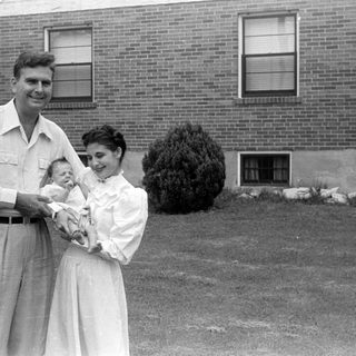 Man, woman, and infant in front of brick house.