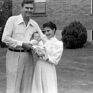 Man, woman, and infant in front of brick house.