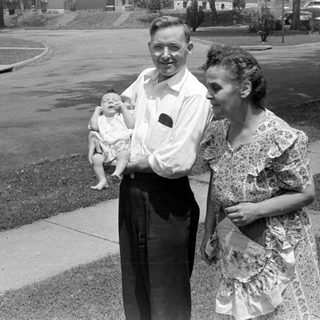 Man and woman with an infant on a sidewalk.