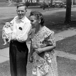 Man and woman with an infant on a sidewalk.