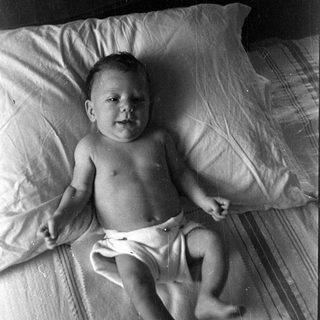 Infant in a diaper lying on a bed.