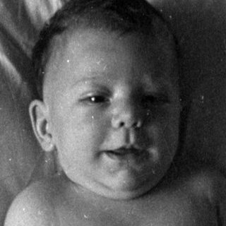 Infant in a diaper lying on a bed.