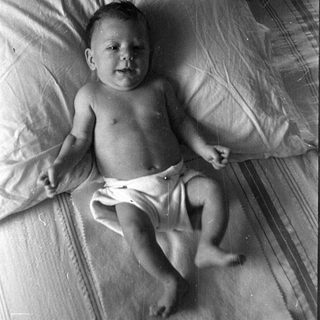 Infant in a diaper lying on a bed.