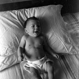 Infant in a diaper lying on a bed.
