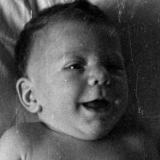 Infant in a diaper lying on a bed.