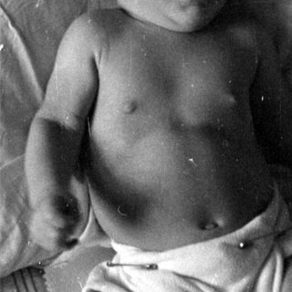 Infant in a diaper lying on a bed.