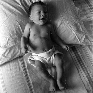 Infant in a diaper lying on a bed.