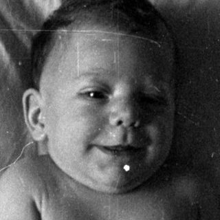 Infant in a diaper lying on a bed.