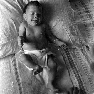 Infant in a diaper lying on a bed.