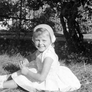 Young girl in white dress sitting outdoors.