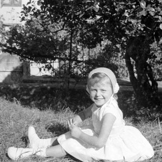 Young girl in white dress sitting outdoors.