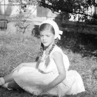 Girl in white dress sitting outdoors by a tree.