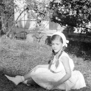 Girl in white dress sitting outdoors by a tree.