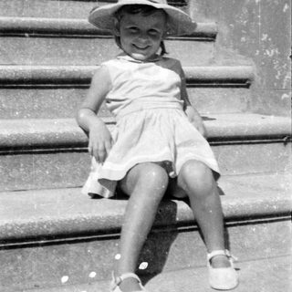 Young girl in sun hat sitting on stone steps.