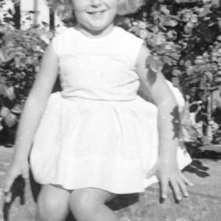 Young girl in a white dress before garden foliage.