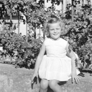 Young girl in a white dress before garden foliage.