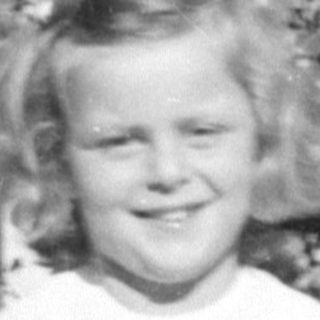 Young girl in a white dress before garden foliage.