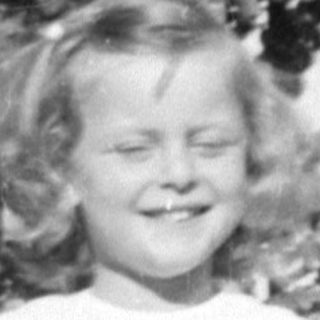 Young girl in a dress standing by a bush.