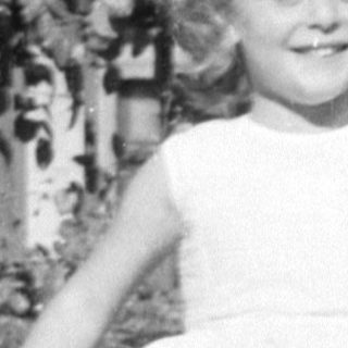Young girl in a dress standing by a bush.
