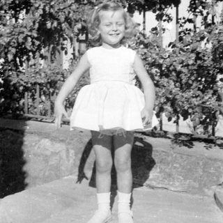 Young girl in a dress standing by a bush.