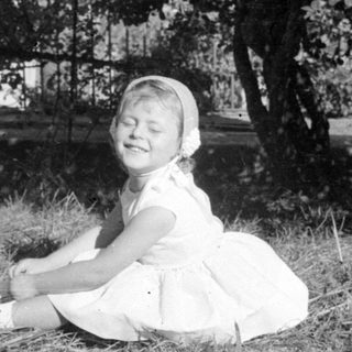 Young girl in white dress sitting on grass.
