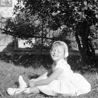Young girl in white dress sitting on grass.