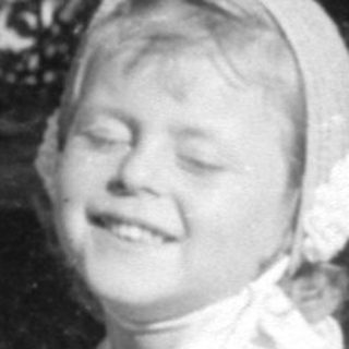 Young girl in white dress sitting on grass.