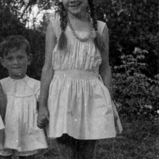 Three children in light dresses standing outdoors.