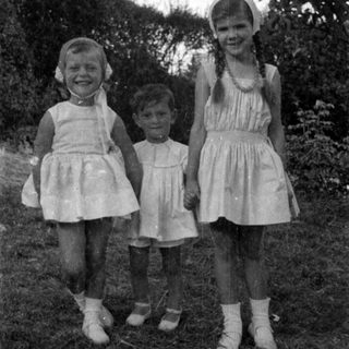 Three children in light dresses standing outdoors.